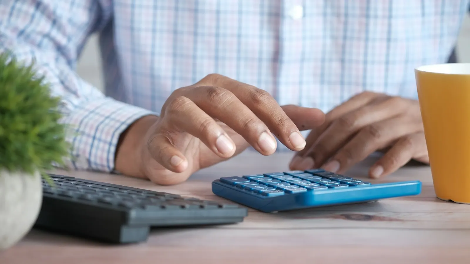 Hands using a calculator at a desk beside a keyboard