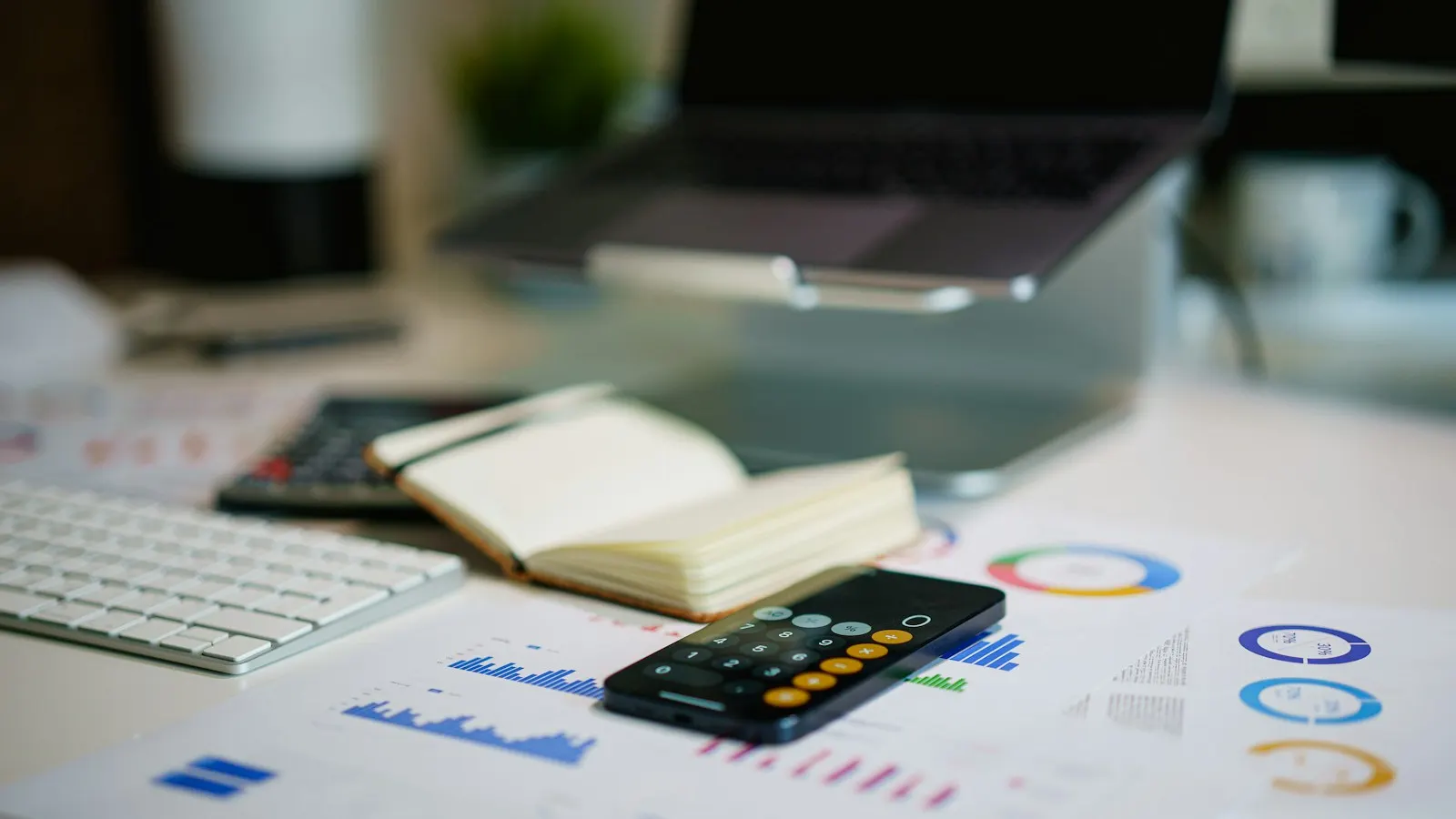 A desk with financial charts, a phone calculator, a notebook and a keyboard
