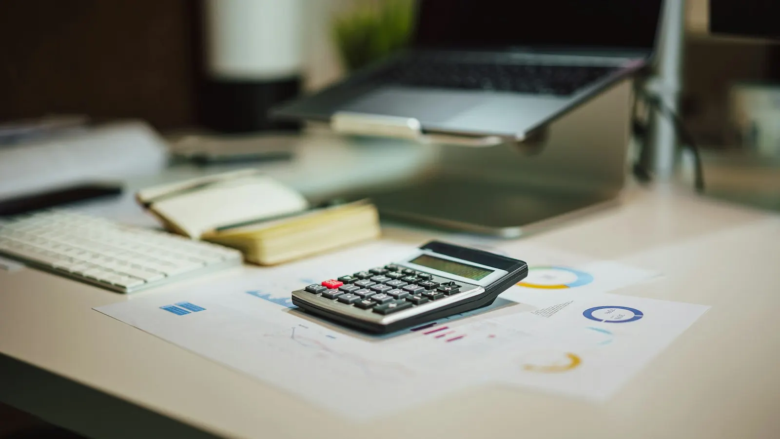An accounting desk with a calculator, laptop and printed charts