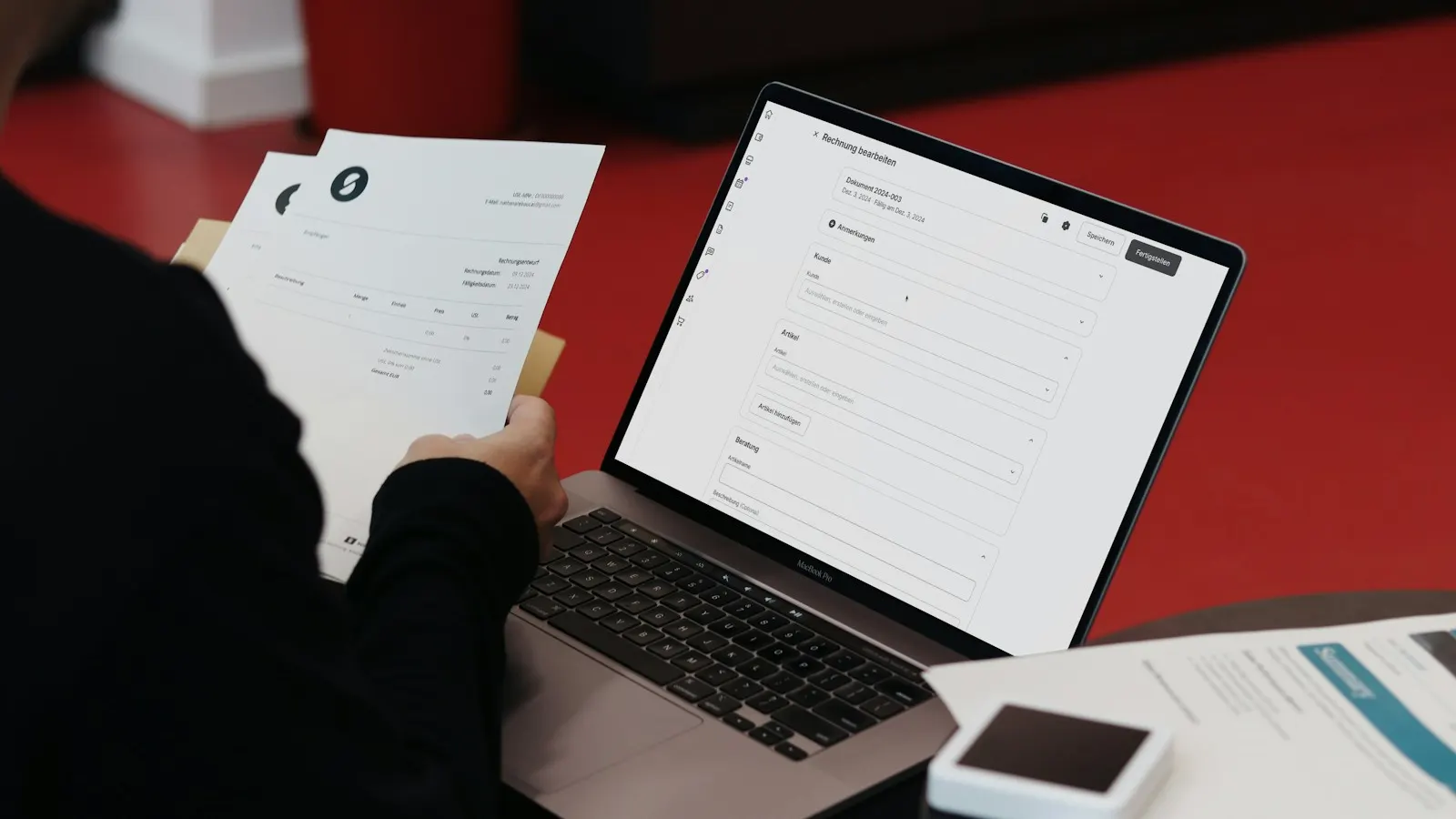 A person reviewing invoices next to an open laptop