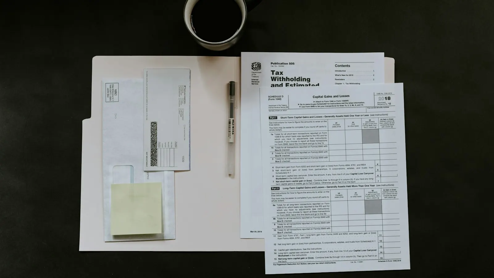 Tax forms, a pen and a coffee mug on a dark desk