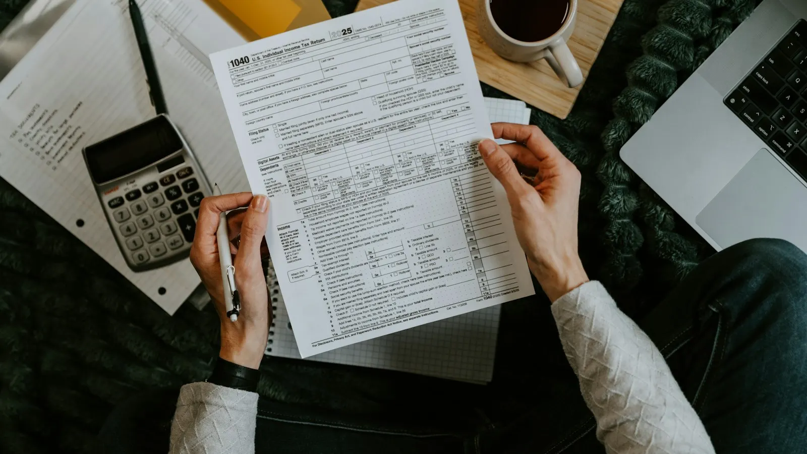 Hands holding tax forms beside a calculator and laptop