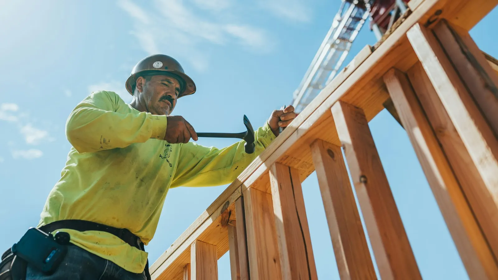 A construction worker in a hard hat framing a wooden structure
