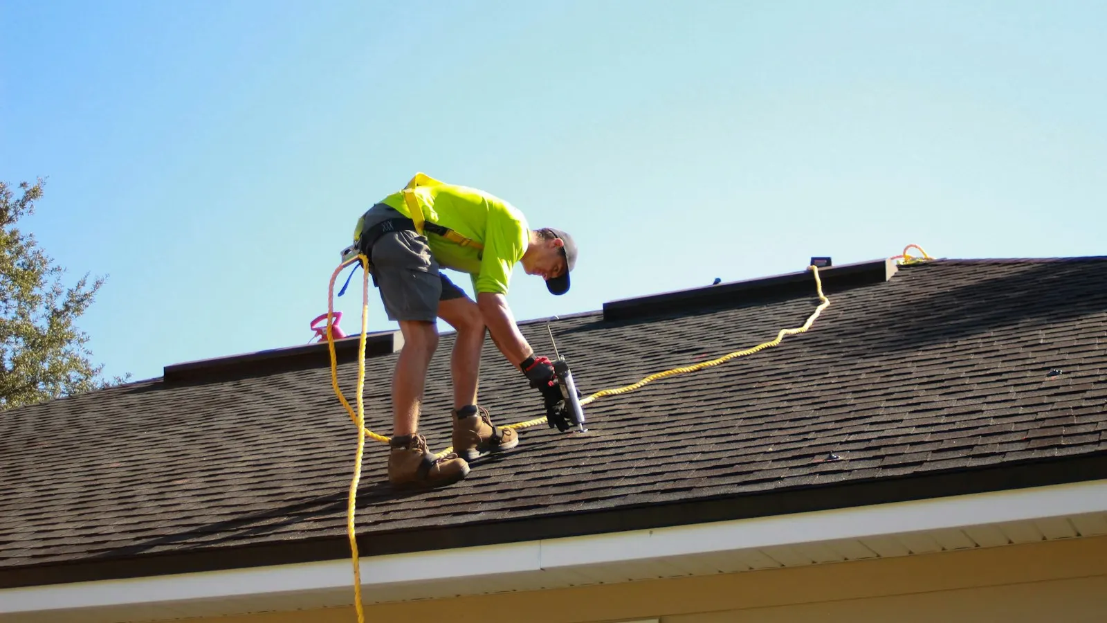 A roofer in a safety harness working on a shingle roof