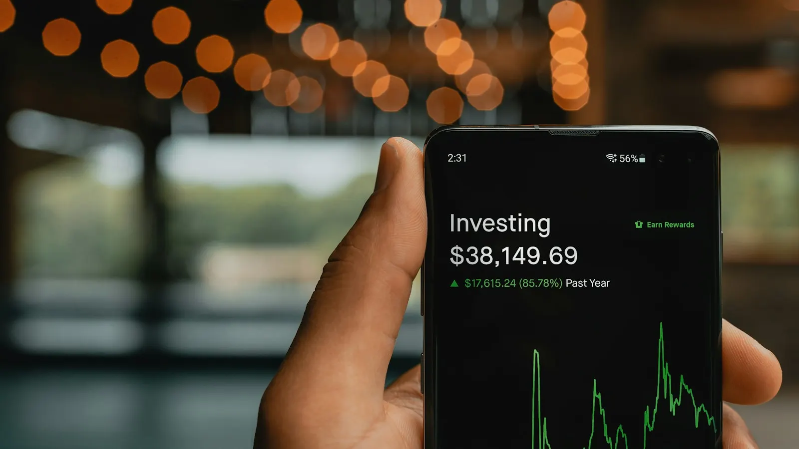 A hand holding a phone showing an investing app balance and chart