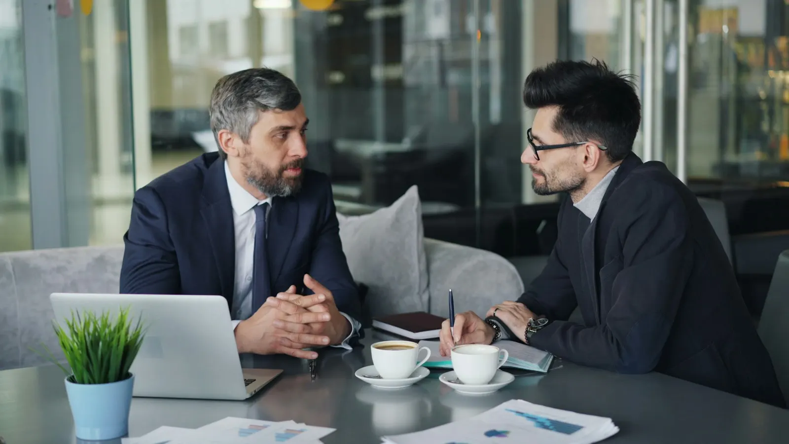 Two men in conversation at a table in a bright office