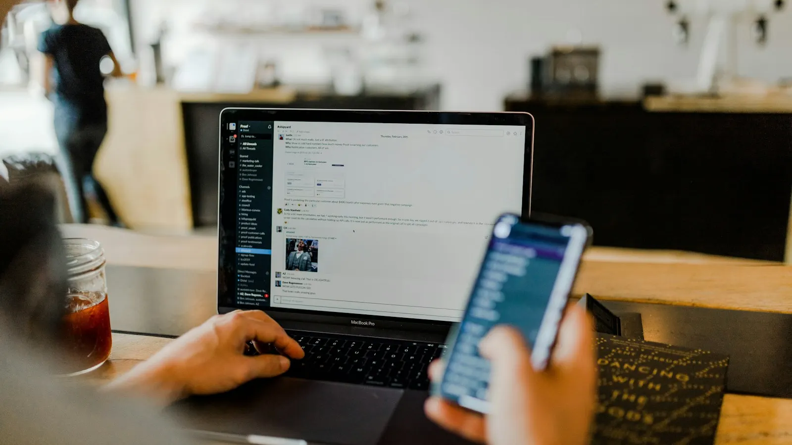 A person using a phone and a laptop at a desk