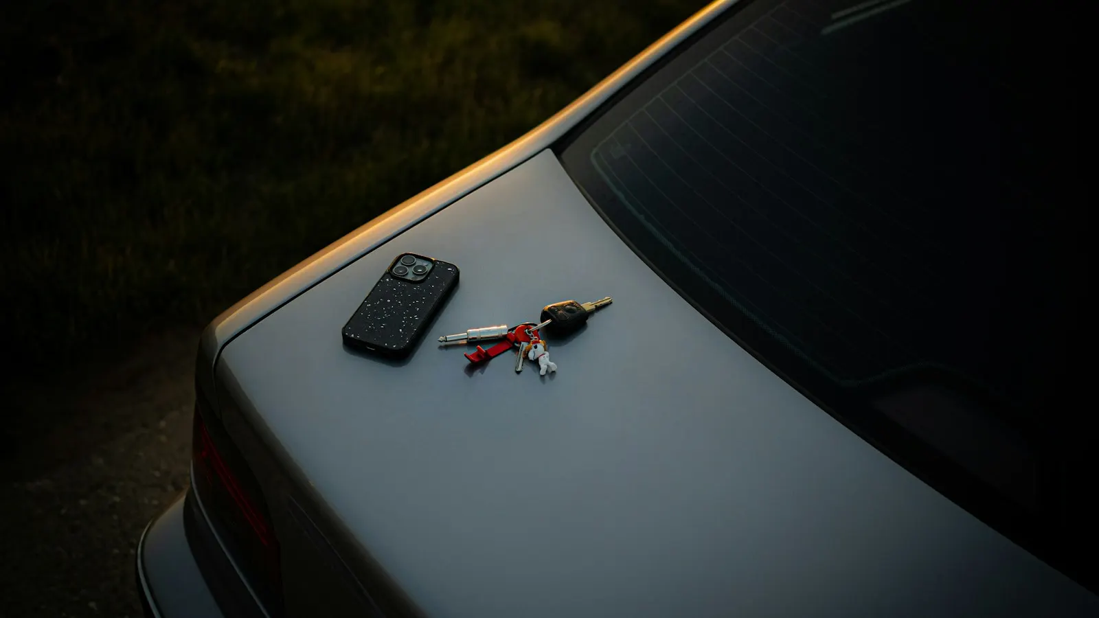 A smartphone and car keys resting on a car trunk at dusk