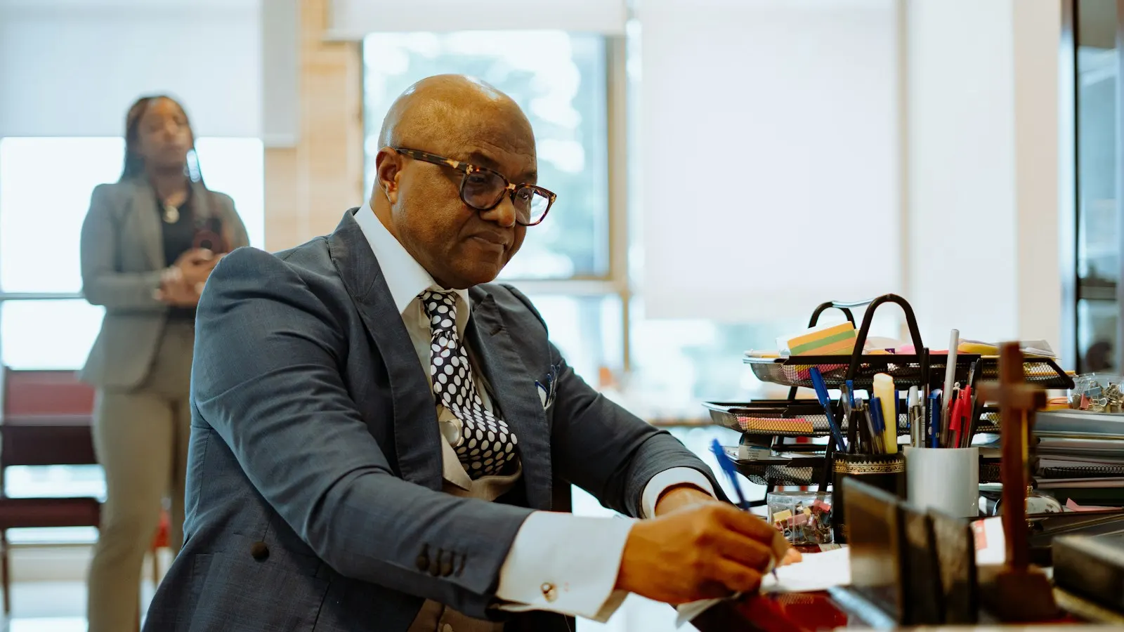 A man in a suit writing at a desk in an office