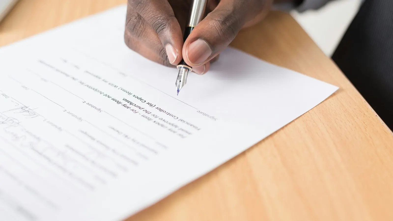 A hand signing a printed document with a pen