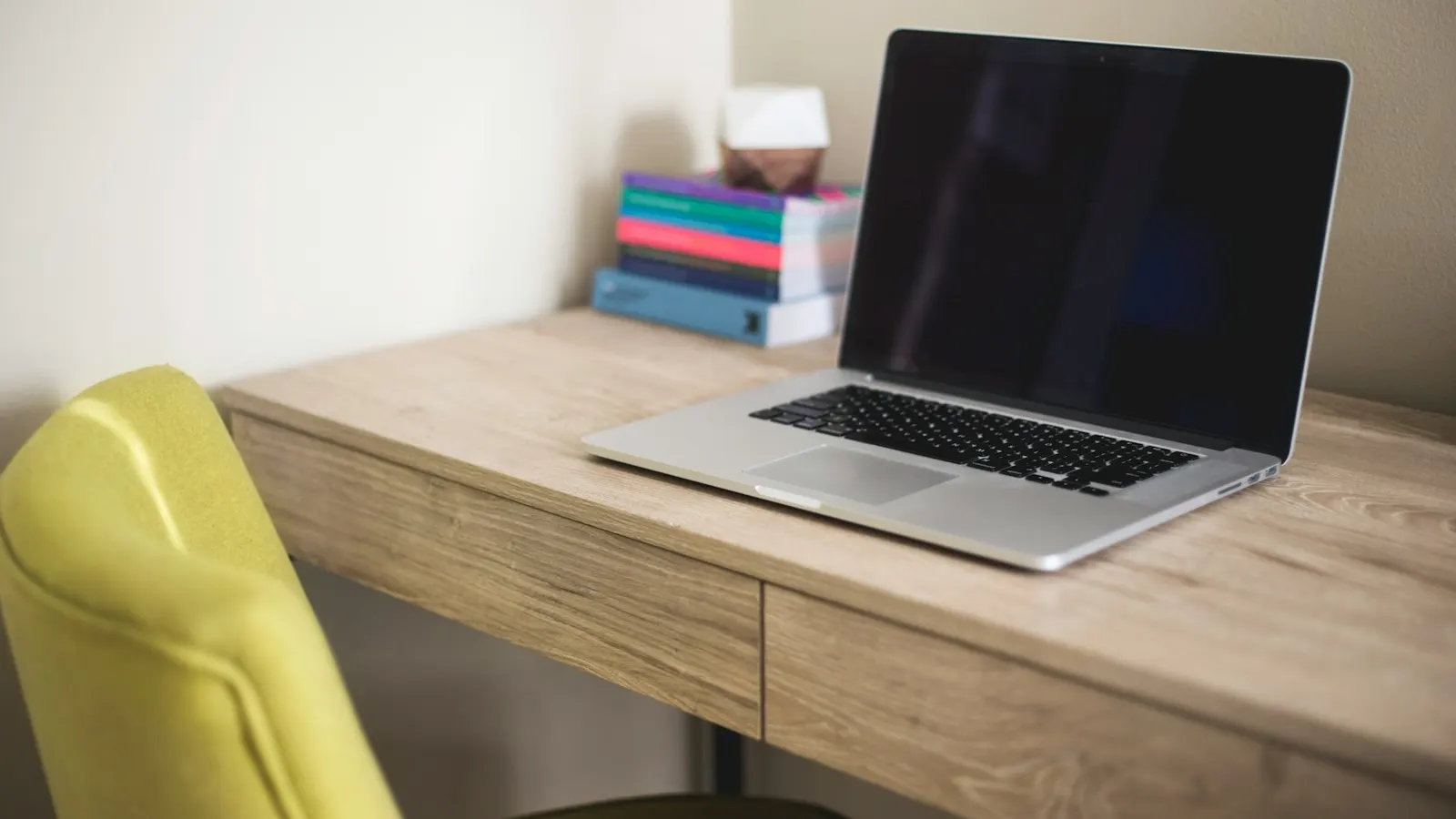 A laptop on a wooden desk beside a stack of books