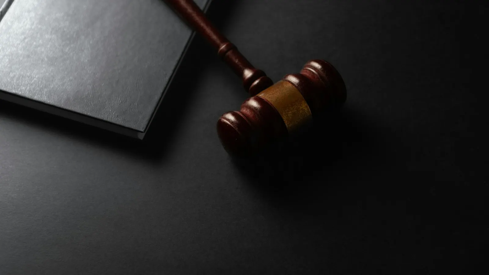 A wooden gavel beside a closed book on a dark desk
