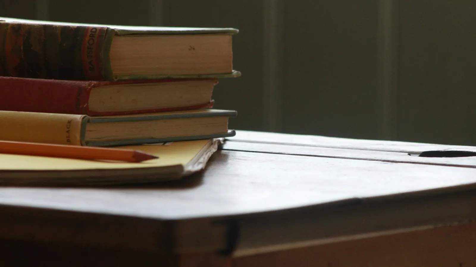 A stack of old books and a pencil on a desk