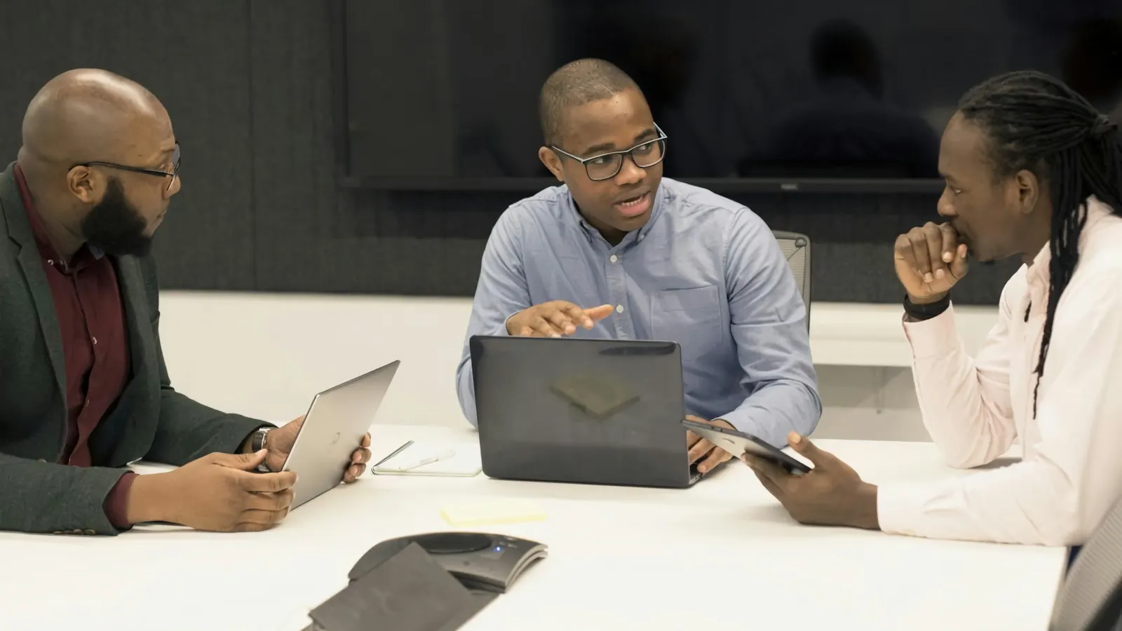 Three professionals working on laptops around a meeting table