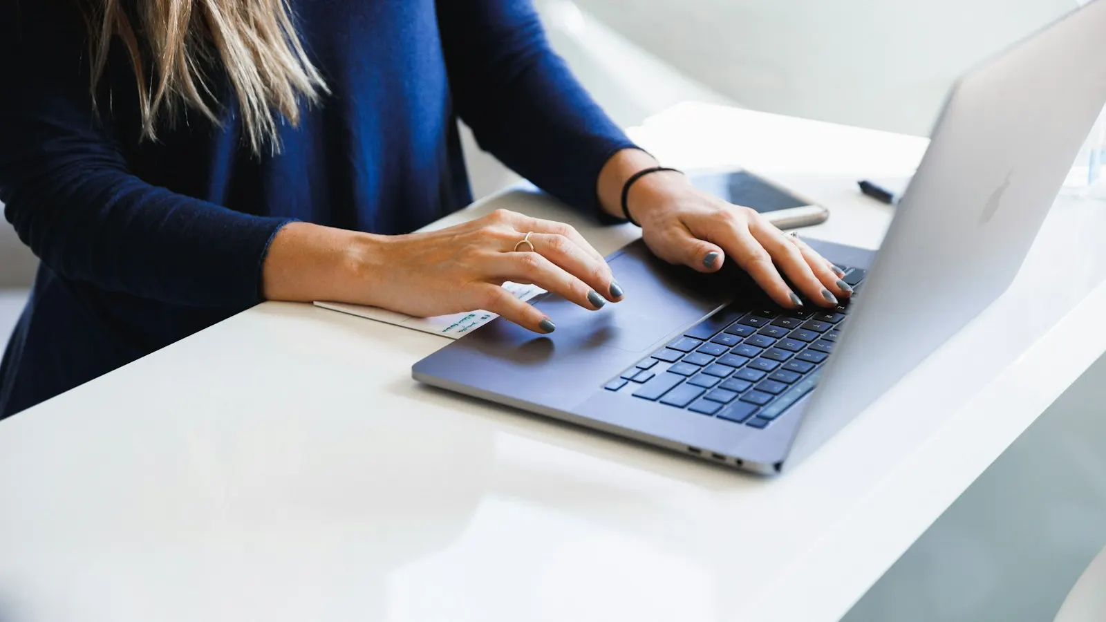 A person typing on a laptop at a white desk