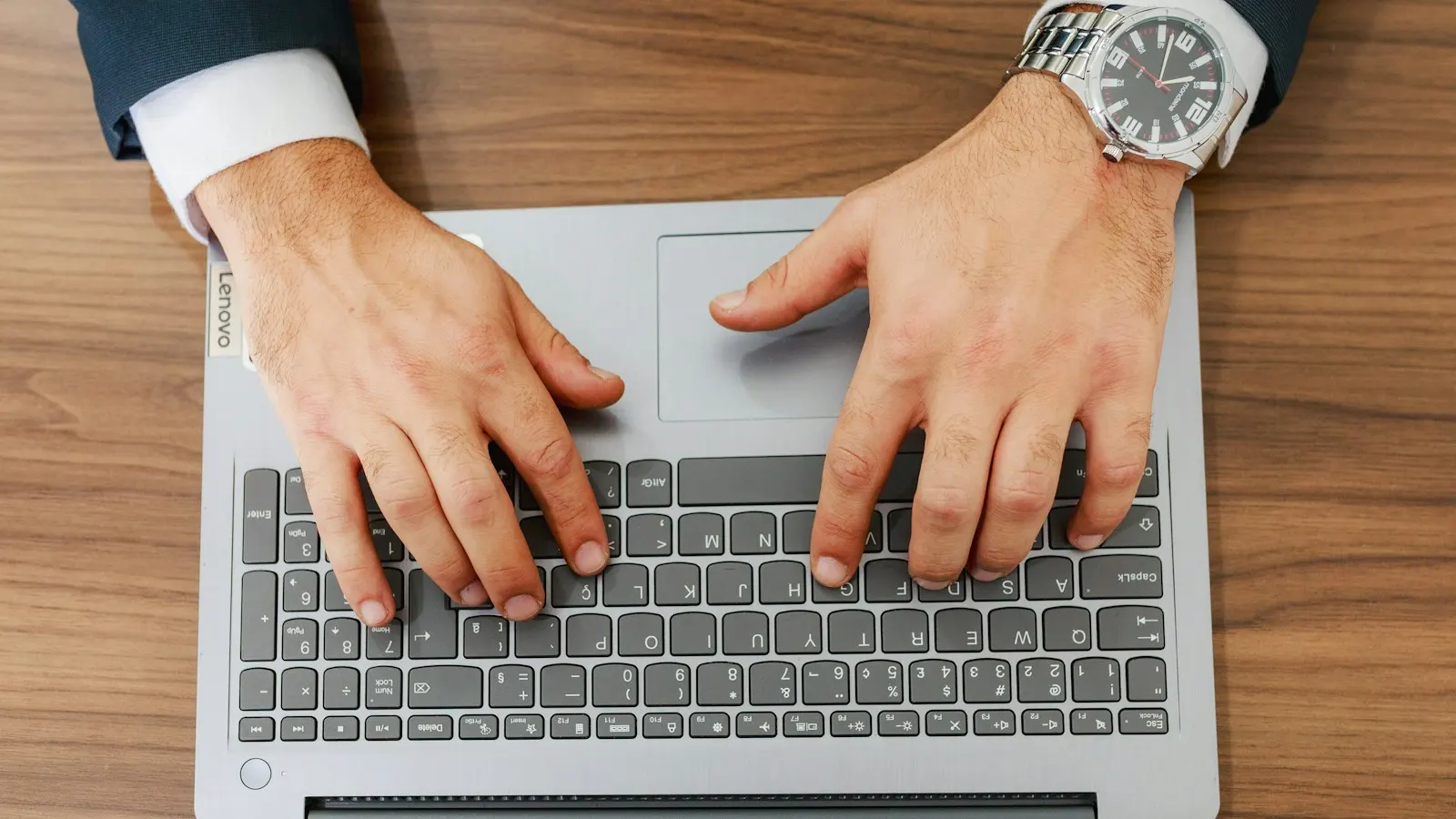 Hands typing on a laptop keyboard on a wooden desk