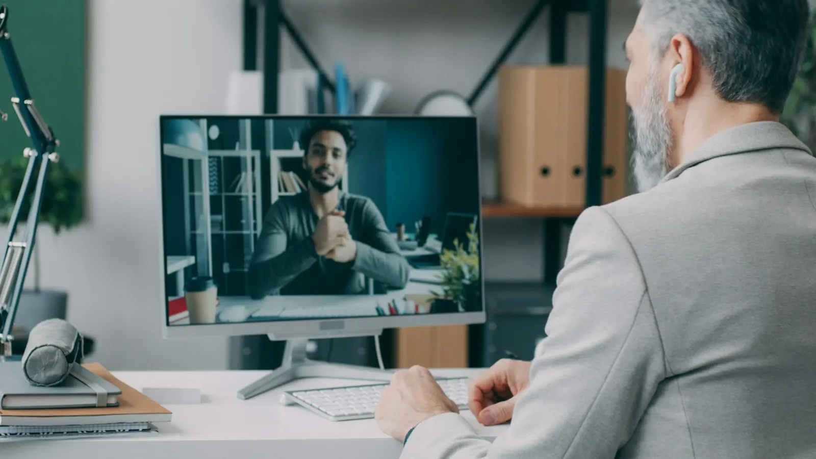 A man on a video call with a candidate shown on his computer screen