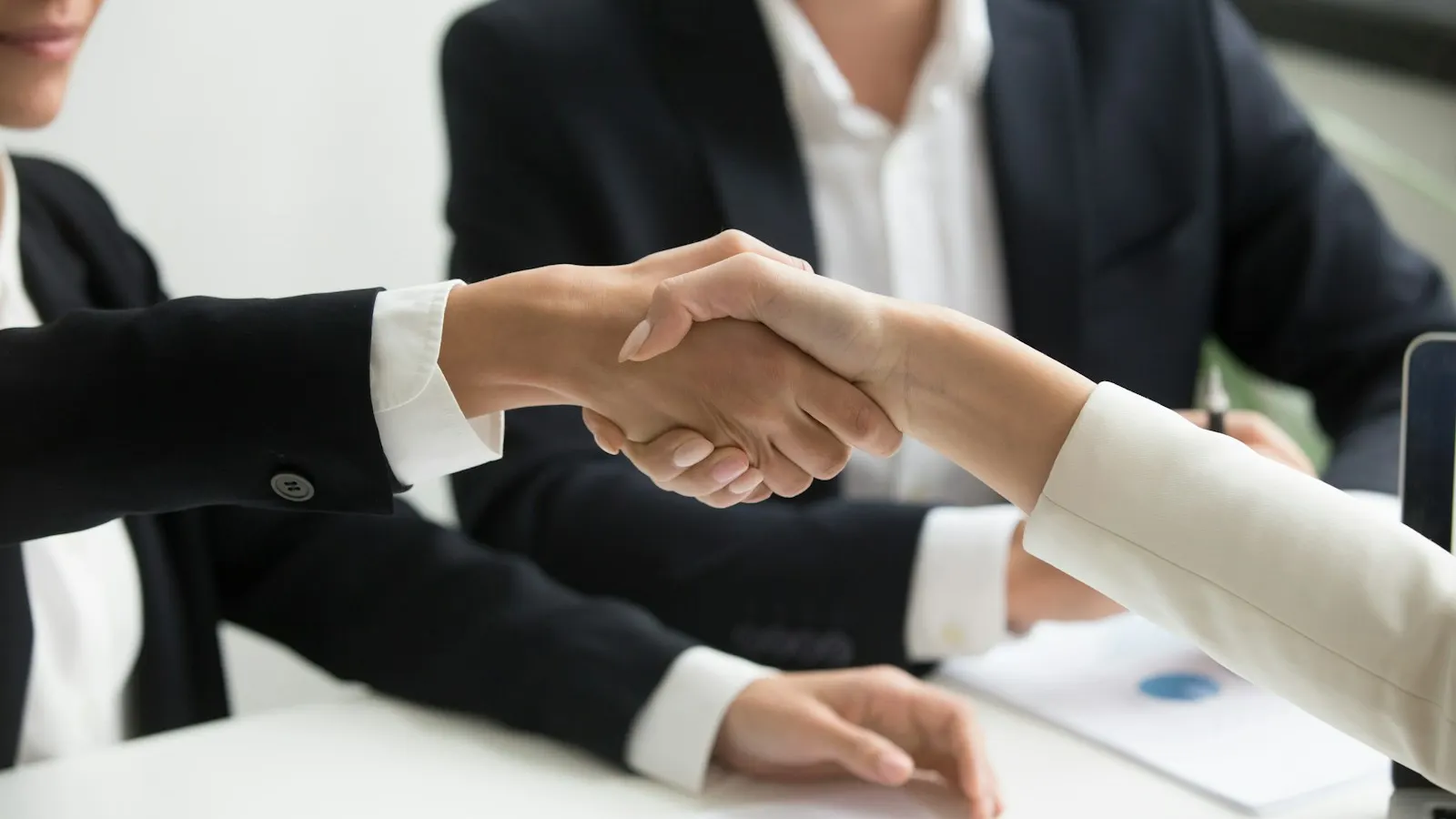 Two people shaking hands across a desk after an interview
