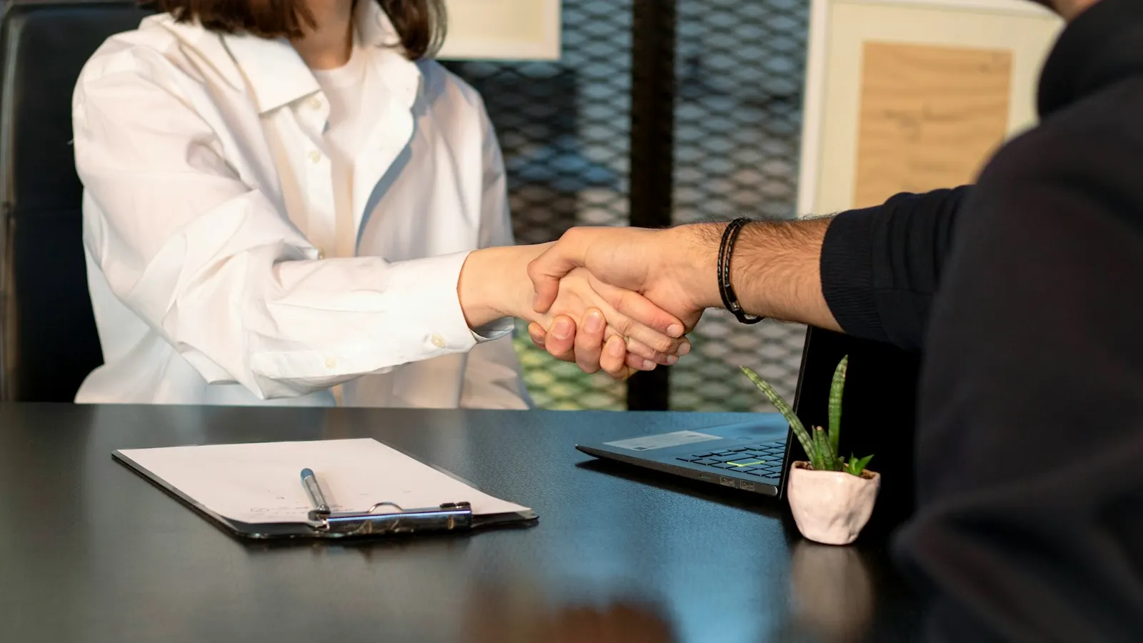 A recruiter shaking hands with a candidate across a desk