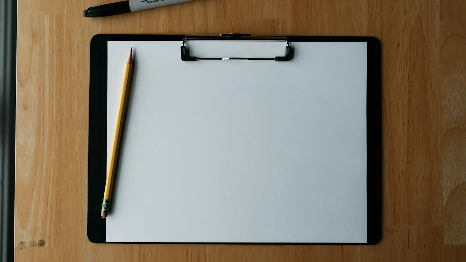 A blank form on a clipboard with a pencil and pen